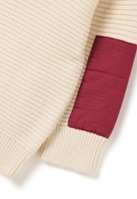 Cremfarbener Strickpullover mit strukturiertem, geripptem Design und kontrastierender bordeauxfarbener Stoffakzent am Ärmel. Weicher, warmerLook.