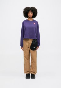 Purple cropped sweatshirt with a red logo patch, beige wide-leg pants, and a black cap with a logo. Black sneakers with laces.