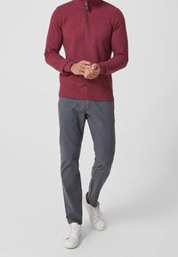 Weinroter Langarm-Zipper-Pullover mit gerippter Textur, kombiniert mit grau gestreiften Hosen und weißen Sneakers. Slim-Fit-Design.