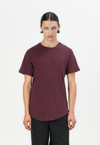 Camiseta de cuello redondo burdeos hecha de tejido suave, con mangas cortas y un dobladillo curvado para un ajuste relajado. Diseño sencillo, sin patrones ni acentos.