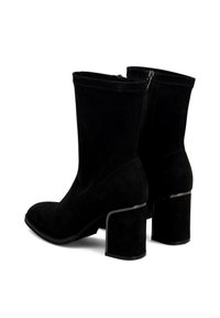 Botas de ante negras hasta la mitad de la pantorrilla con tacones de bloque, cremalleras laterales y un sutil borde plateado en el borde del tacón, mostradas desde un ángulo trasero.