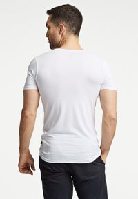 Biała koszulka t-shirt z krótkim rękawem, wykonana z miękkiego materiału, o dopasowanym kroju i okrągłym dekolcie, pokazana z tyłu.
