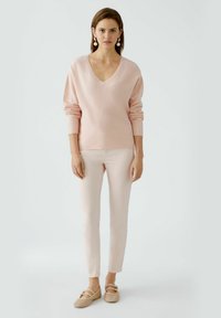 Light pink knit sweater with a V-neck, long sleeves, paired with pale pink fitted pants and beige shoes featuring two straps across the top.