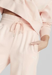 Pantalones de chándal rosa claro con cintura ajustable, bolsillos laterales y pequeño logotipo blanco. Fabricados en una suave tela texturada con un corte relajado.