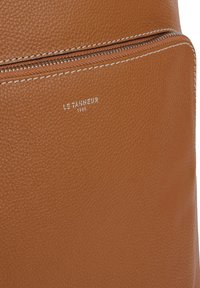 Zaino in pelle marrone con superficie testurizzata, tasca frontale con zip e marchio in rilievo. Mette in risalto i dettagli delle cuciture e un design elegante.
