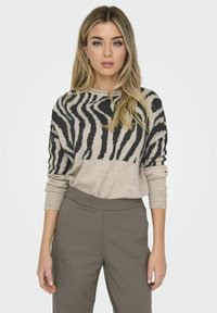 Suéter a rayas en beige y negro con un corte holgado y puños acanalados, combinado con pantalones de tiro alto en un marrón claro sólido.