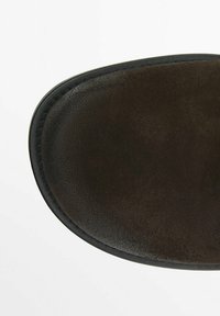 Botte en daim marron avec un bout arrondi, une texture lisse et une semelle en caoutchouc noir. Présente des coutures détaillées le long du bord.