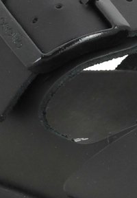 Sandal nero con una fascia spessa e liscia con perforazioni, lati aperti e una suola texturizzata. Design semplice e minimalista.
