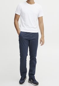 Vit bomull t-shirt i kombination med marinblå lätta byxor. Sneakers med mörkblå detaljer och en grå sula. Enkel, ren design.