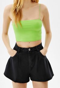 Shorts de mezclilla negra de cintura alta, con bolsillos delanteros y un botón plateado como detalle. Combinados con un top corto ajustado de color verde brillante con tirantes delgados.