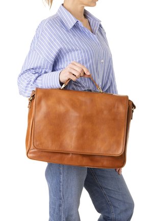 Persoon met een blauw gestreept shirt en spijkerbroek die een grote bruine leren aktetas vasthoudt bij het handvat ter hoogte van de taille.