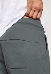 Calças de suéter cinzentas com uma textura suave, apresentando dois grandes bolsos nas costas e uma cintura elástica para um ajuste ajustável.