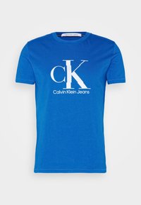 Královsky modré bavlněné tričko s velkým bílým logem "CK" a textem "Calvin Klein Jeans". Krátké rukávy a design s kulatým výstřihem.