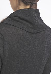 Schwarzer Strickpullover mit einem Schalkragen, der eine subtile schimmernde Textur und ein enganliegendes Design aufweist, das die Weichheit des Materials betont.