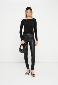 Črn dolgi rokav s raztresenimi okraski, združen z sijočimi črnimi hlačami s visokim pasom in čevlji z pikicami na naramnicah. Drži črno torbico.