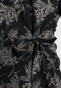 Schwarzes Kleider aus Stoff mit floralem Muster, das weiße und beige Punkte zeigt, tailliert, mit einer gebundenen Schleife als Styling-Detail.