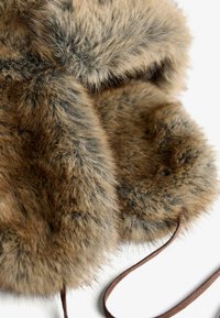 Barna tónusú műszőrme sapka puha, sűrű textúrával. Kerek fülvédőkkel és barna bőrszerű pánttal rendelkezik a biztonságos rögzítés érdekében.