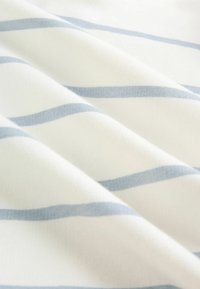 Bombažno blago z mehko teksturo in premenjujočimi se belimi in svetlo modrimi vodoravnimi črtami. Nežni prepogibi ustvarjajo dinamičen videz.