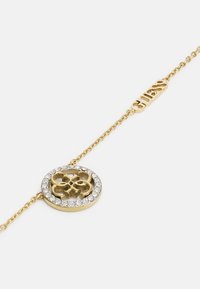 Guld armbånd med en cirkelvedhæng med udsparingsdesign omkranset af klare rhinsten. Kæden har en slank, delikat struktur.