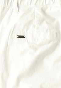 Valkoinen puuvillakangas, jossa on sileä pinta, ja takataskussa on hopeinen tagi, johon on kaiverrettu "FRENCH CONNECTION."