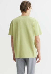 Jasnozielona koszulka z krótkim rękawem o luźnym kroju, z okrągłym dekoltem i gładką fakturą. Tylny widok ukazuje prosty design.