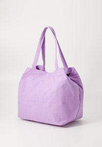Stor lila axelväska i canvas, med två kraftiga handtag och en mjuk, flexibel form. Ingen synlig hårdvara eller detaljer.