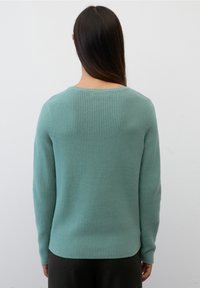 Lys teal ribbet trøje med lange ærmer og en bred rund halsudskæring, med en let buet kant bagpå.