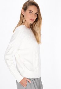 Pulover alb tricotat cu modele texturate, guler rotund și manșete cu elastic. Asortat cu o fustă gri deschis.