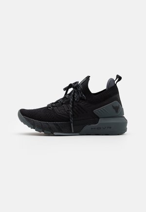 Zapatilla deportiva negra y gris con parte superior de tejido, cordones con patrón, suela acolchada y logo en el talón, aislada sobre un fondo blanco.