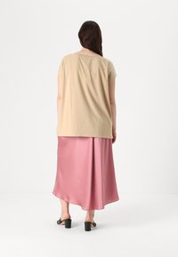 Beige bomullströja med korta ärmar, kombinerad med en lång rosa satängkjol och svarta klacksandaler med blockklack, sedd bakifrån.