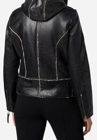 Giacca nera in pelle con cappuccio, cuciture bianche a contrasto, taglio aderente, dettagli con cerniere sulle maniche e texture liscia.