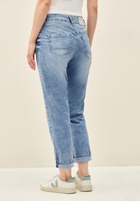 Jeans en denim bleu clair avec une coupe décontractée, finition avec des ourlets retroussés et deux poches arrière. Associés à des baskets blanches avec des accents gris.