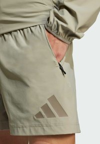 Lys beige shorts med en tekstureret overflade, elastisk talje, sidelomme med sort lynlås og et diskret mørkt logodesign.