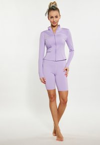 Set sportiv de culoare violet deschis, compus dintr-un top cu mânecă lungă și fermoar și pantaloni scurți ajustați, fabricat dintr-un material neted și elastic.