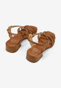 Sandalias de cuero marrón con múltiples correas y un tacón grueso. La plantilla presenta un logotipo y la suela tiene un patrón de madera texturizada.