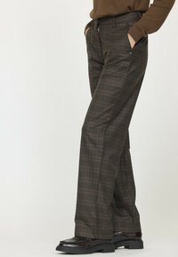 Pantalons à carreaux marron avec une coupe décontractée, des poches avant et une texture lisse, associés à des chaussures en cuir noires et un haut marron.