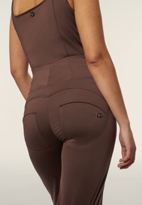 Leggings marroni realizzati in tessuto liscio e elastico. Presentano un vita alta e due tasche posteriori. Un piccolo logo si trova sopra la tasca destra.