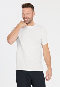 Biała bawełniana koszulka z krótkim rękawem i okrągłym dekoltem, noszona przez mężczyznę. Charakteryzuje się gładką strukturą i luźnym krojem.