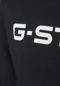 Zwart fabric met witte "G-S" tekst prominent weergegeven. Soepele textuur, aansluitend ontwerp, met een eenvoudige moderne esthetiek.