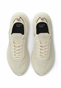 Μπεζ αθλητικά παπούτσια με επάνω μέρος από δίχτυ, στρογγυλή μύτη και υφή καουτσούκ στη σόλα. Διαθέτουν ελαστικά κορδόνια και λογότυπο στη γλώσσα του παπουτσιού.