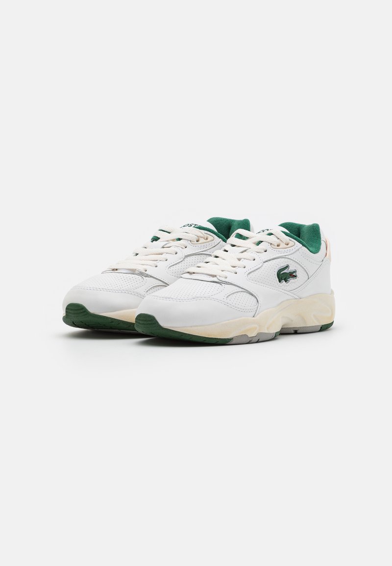 Zapatillas blancas con acentos verdes, con parte superior perforada, suela texturizada y forma redondeada. Cuerdas y marca en el lateral.