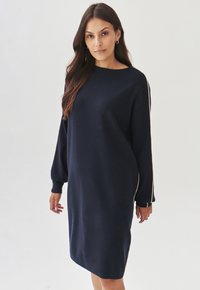 Robe pull bleu marine à la coupe décontractée, avec des manches longues et des poignets côtelés. Présente un col rond et des accents latéraux blancs. Texture douce.
