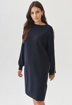 Navy blue sweater dress with a relaxed fit, long sleeves, and ribbed cuffs. Features a round neckline and white side accents. Soft texture.