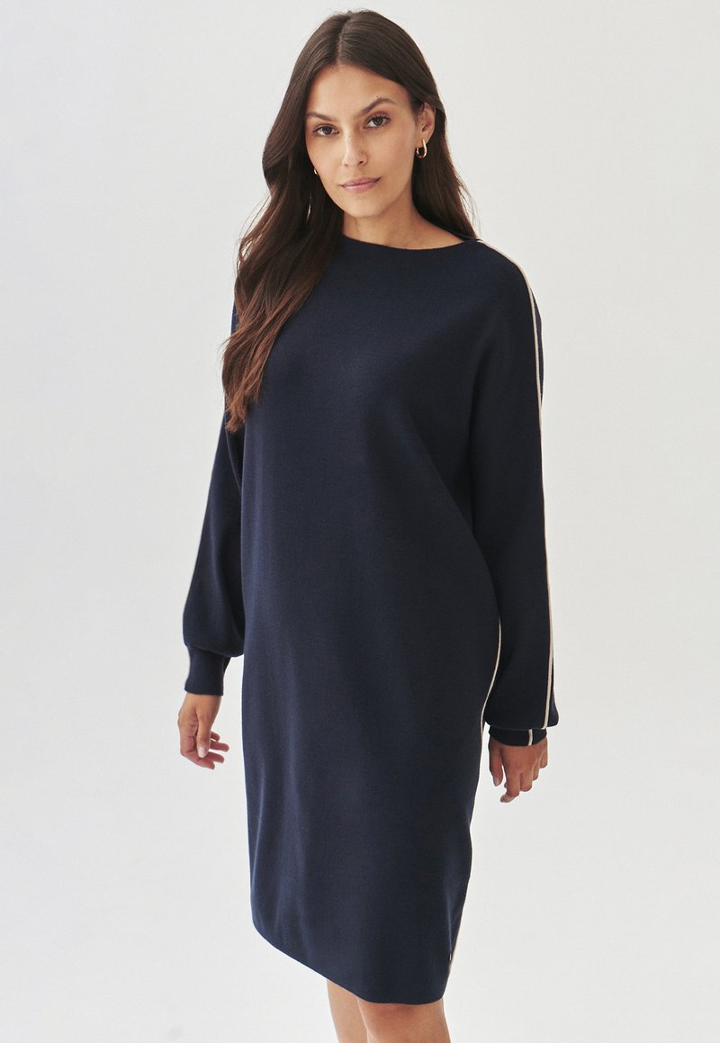 Robe pull bleu marine à la coupe décontractée, avec des manches longues et des poignets côtelés. Présente un col rond et des accents latéraux blancs. Texture douce.