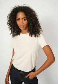 Short-sleeved cream t-shirt made of soft fabric; round neck, relaxed fit, paired with dark denim jeans. Smooth texture with minimal details.