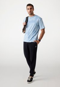 Tricou scurt cu mânecă, de culoare albastru deschis, cu un grafic texturat, asortat cu joggeri negri cu un logo. Teniși negri completează ținuta.