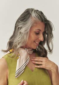 Svetloroza svilena ruta s črnimi črtami in rumenimi poudarki, nošena okoli vratu, v kombinaciji z zeleno brezrokavno majico z V-izrezom.