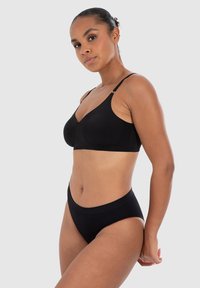 Sujeta negro inalámbrico con tirantes ajustables y tela suave. Ropa interior negra de tiro alto con textura acanalada. Diseño minimalista.