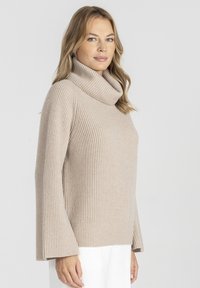 Beżowy sweter typu golf z żeberkową teksturą, posiadający szerokie rękawy i luźny krój. Lekka tkanina zapewnia komfort i możliwość warstwowania.