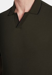 Oliwkowa koszulka polo z teksturowanej tkaniny, z dekoltem w serek wykończonym ciemnonawigacyjnym obszyciem oraz klasycznym dopasowanym krojem.